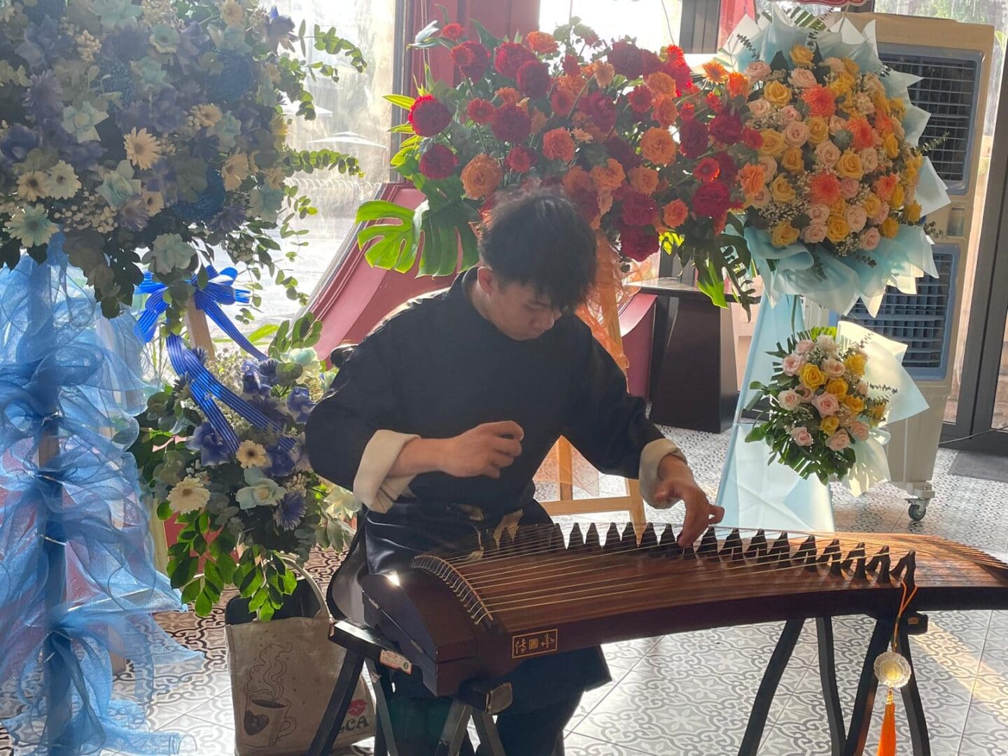 Man playing guzheng with flower arrangements.